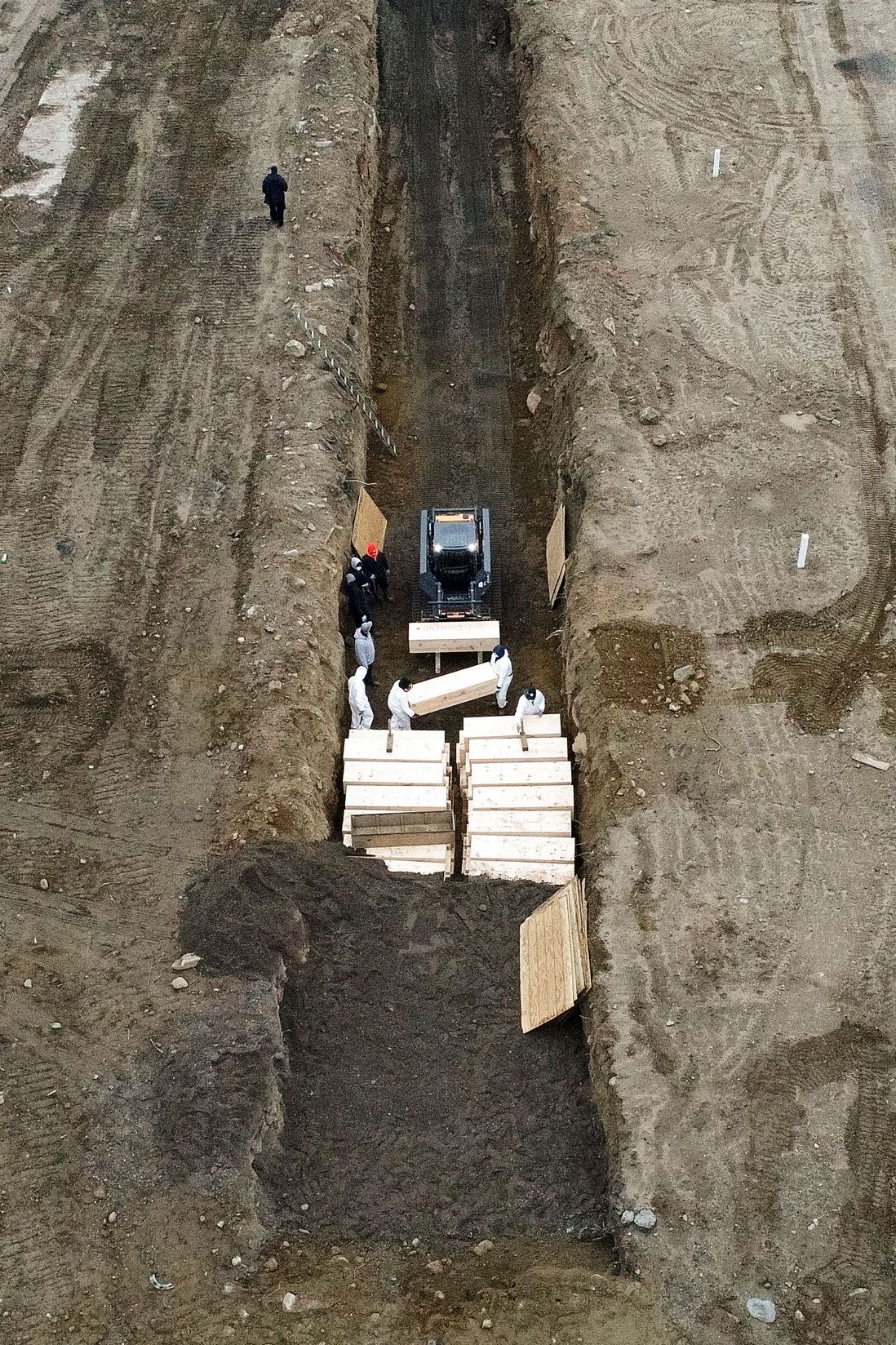 Workers wearing personal protective equipment bury bodies in a trench on Hart Island, in the Bronx on April 9, 2020.